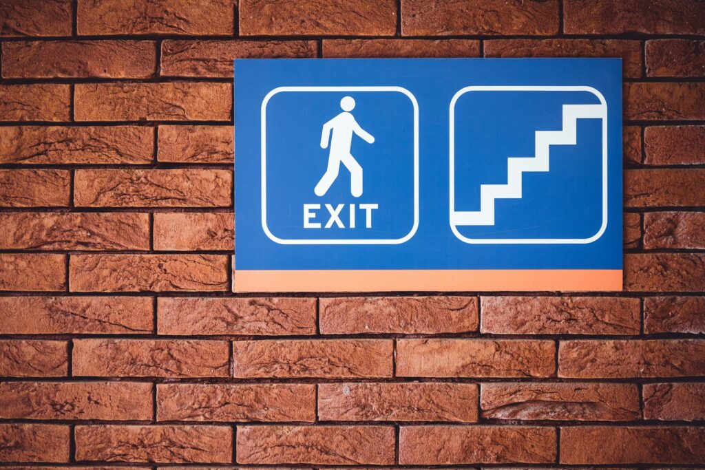 blue and white exit signage mounted on brown brick wall