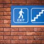 blue and white exit signage mounted on brown brick wall